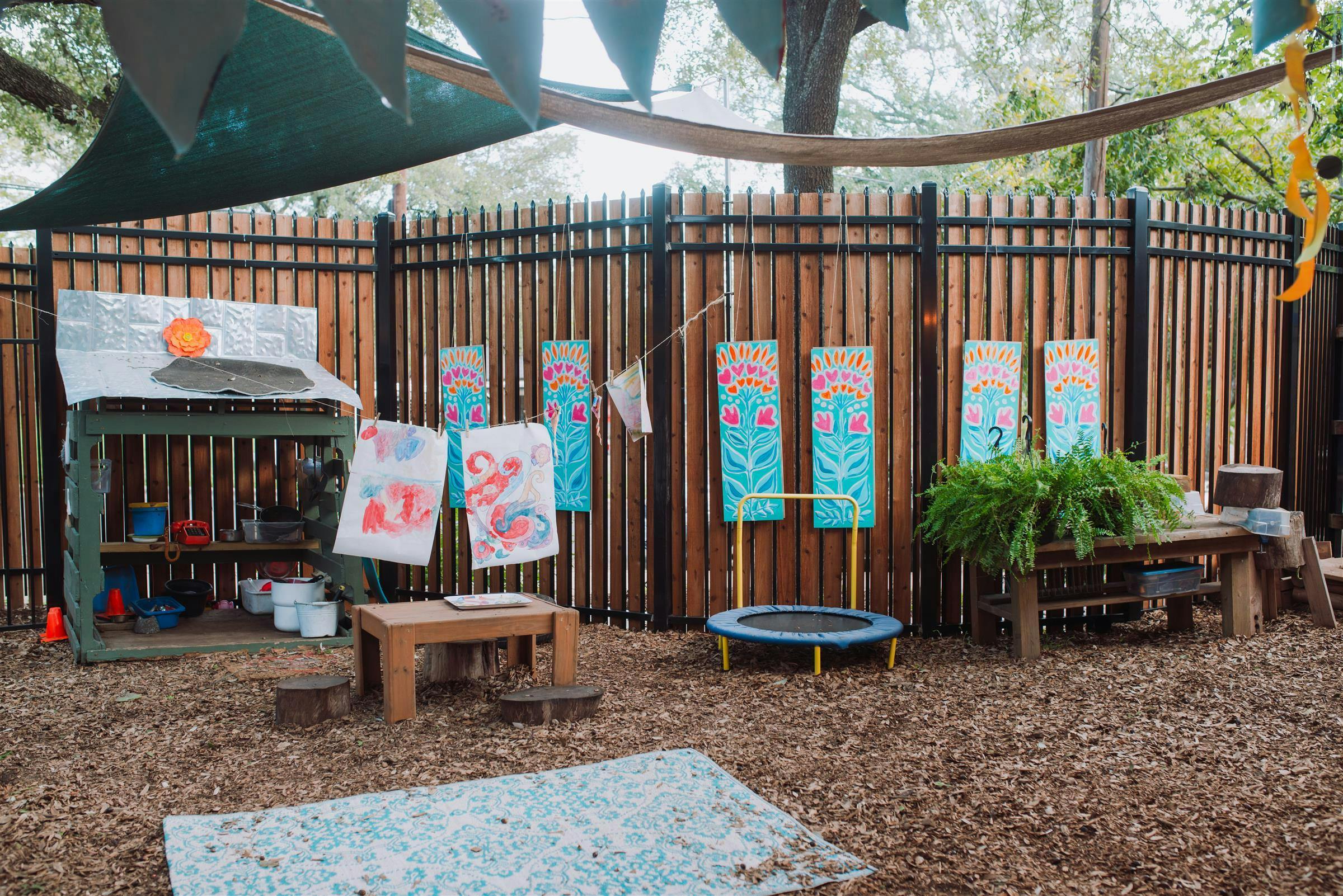 Outdoor play area with a wooden fence, play kitchen, and small trampoline