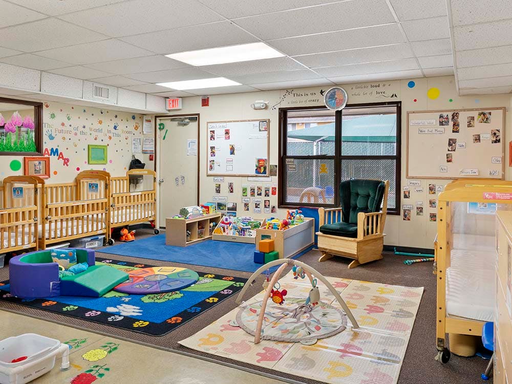 Classroom with multiple cribs, a rocking chair, and play mats with toys