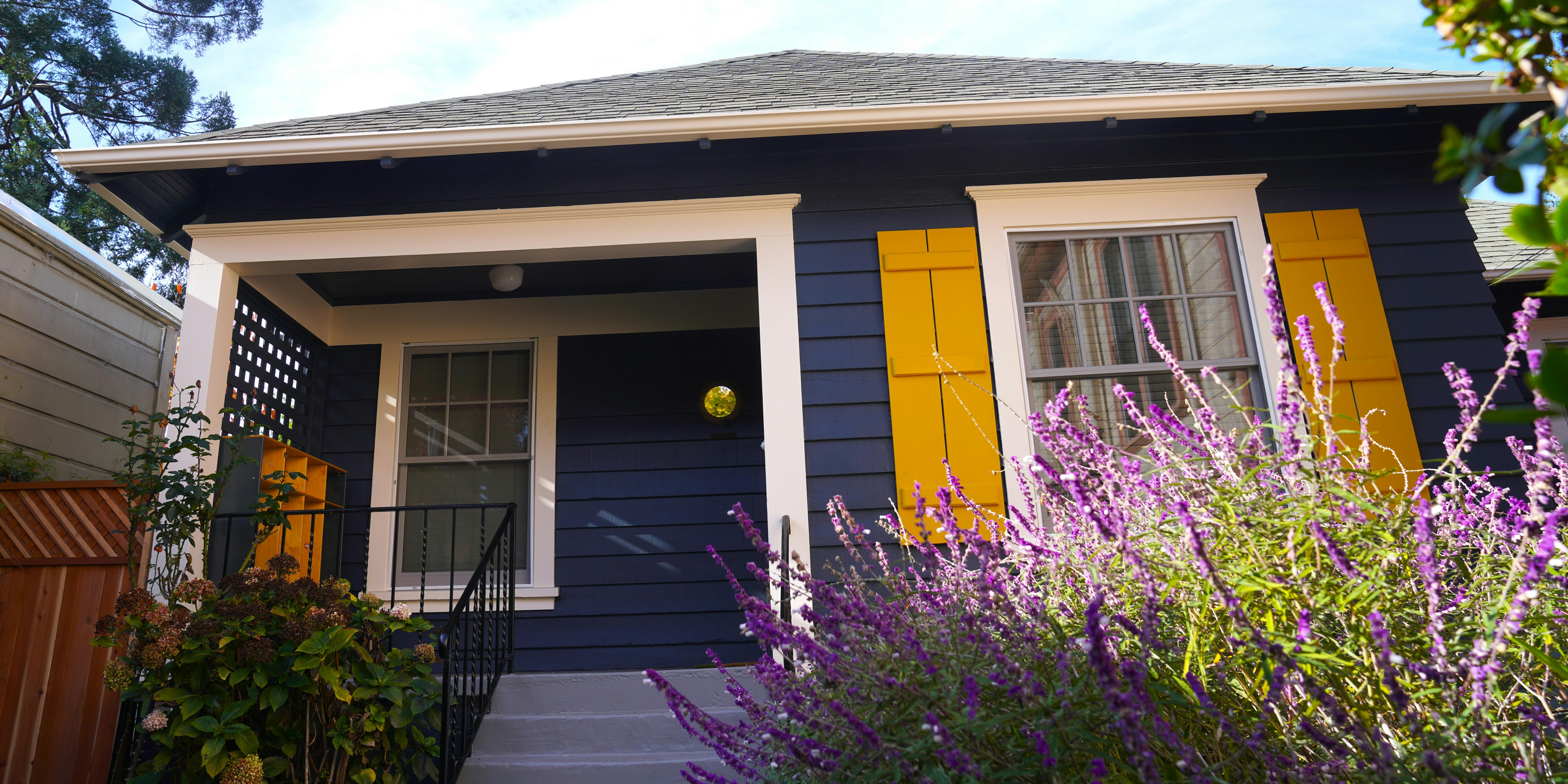 House with dark siding, white trim, yellow shutters, and purple flowers