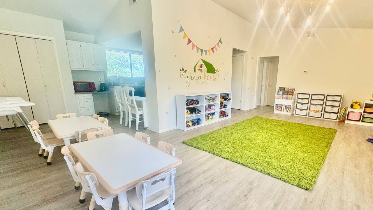 Playroom with small tables and chairs, green rug, and toy shelves