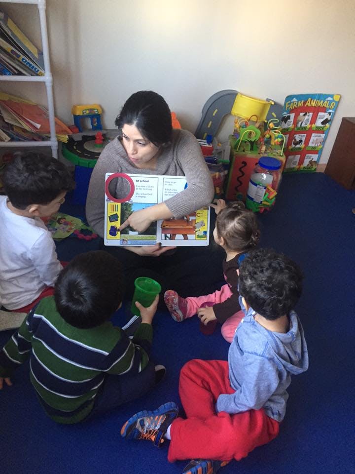Person reading a book to four children sitting on the floor