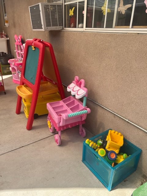 Children's easel, pink toy shopping cart, and blue bin of toys