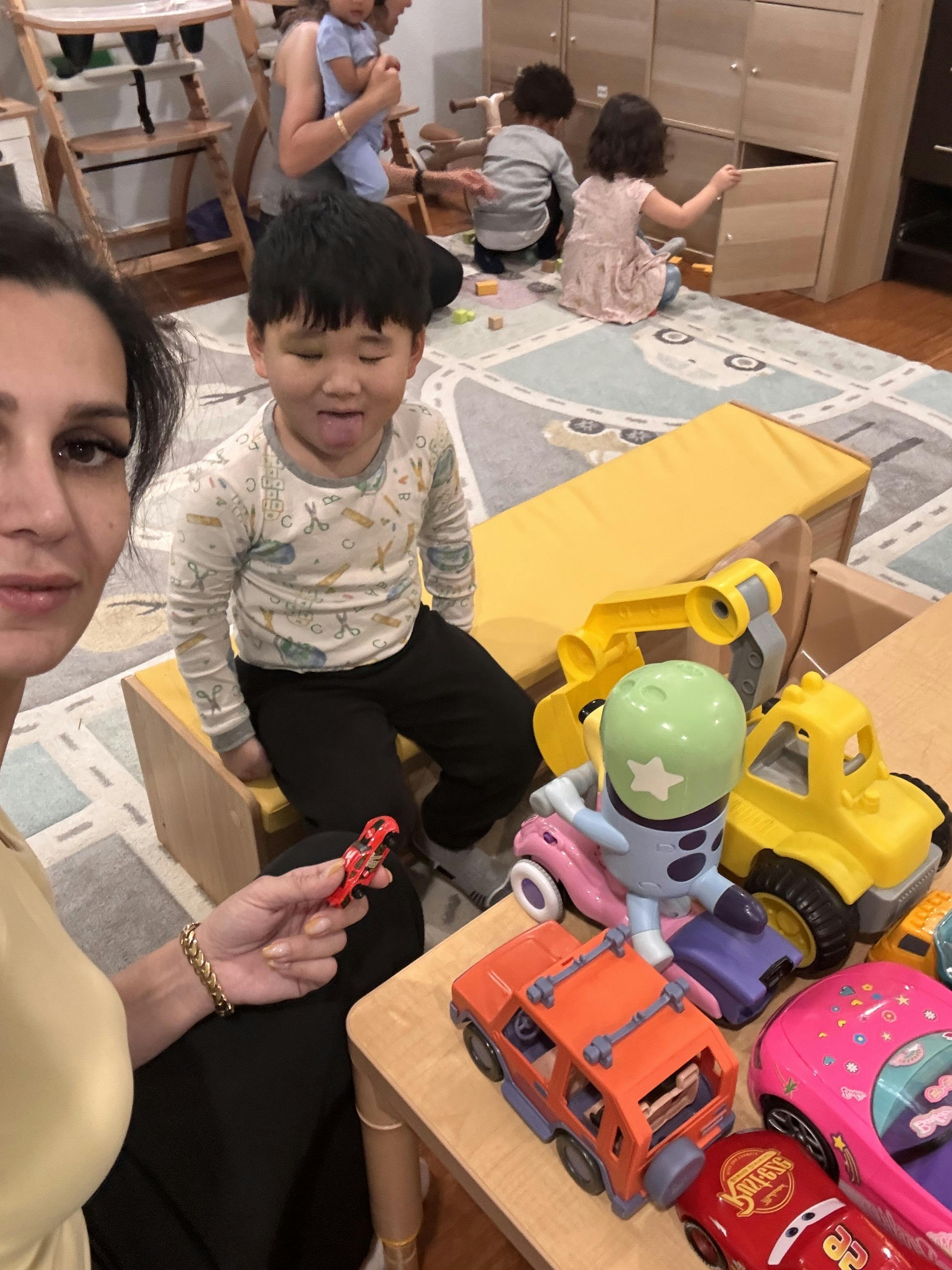 A person holding a toy car near a child sitting on a bench in a playroom