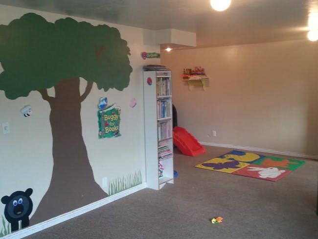 Playroom with tree mural, bookshelf, red slide, and colorful floor mat
