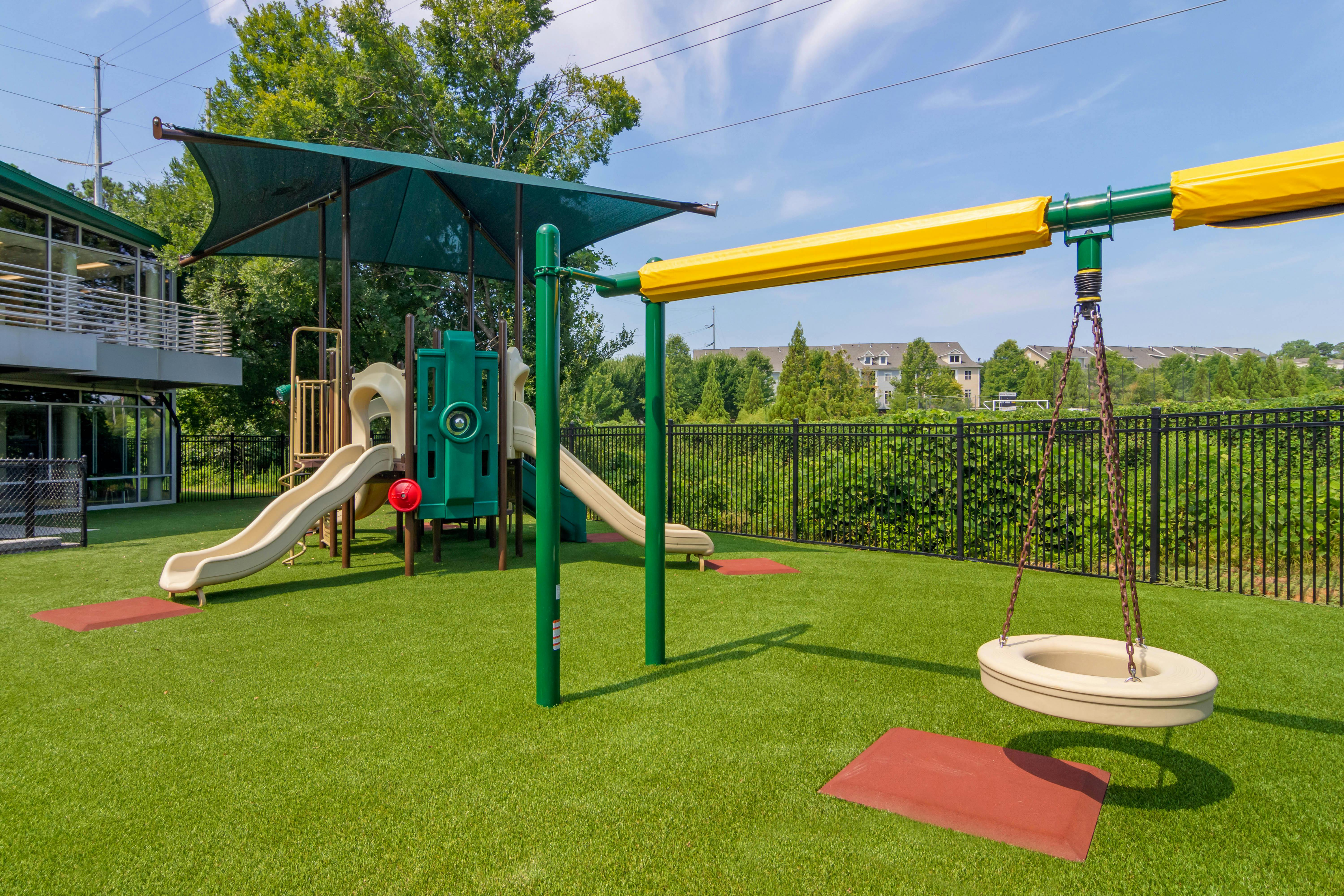A modern playground with multiple slides, swings, and green turf flooring