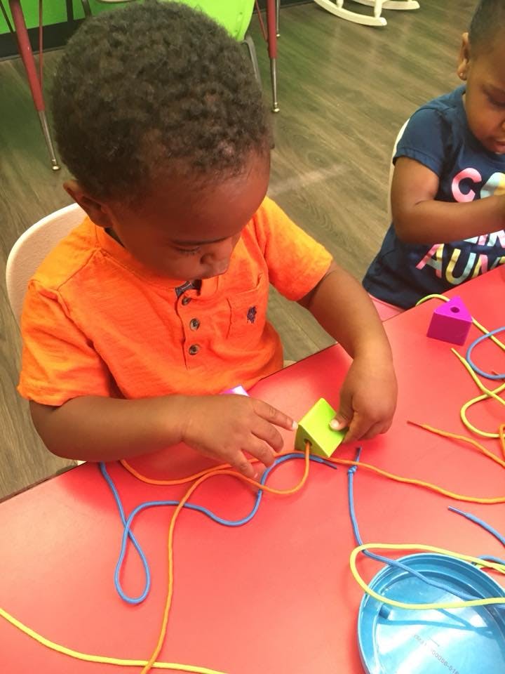 Child playing with lacing beads and string at a table