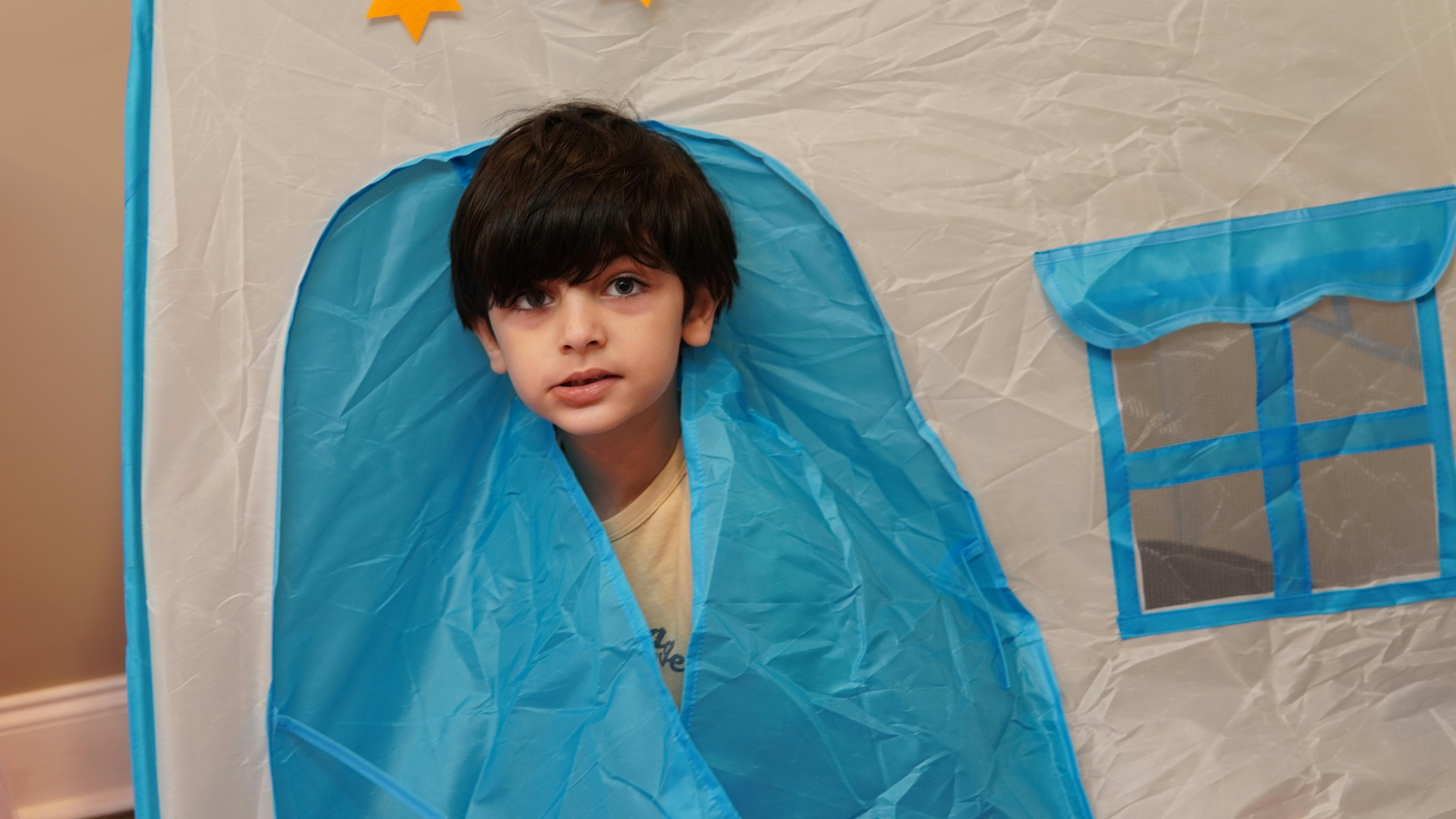 Child looking out from a blue and white play tent