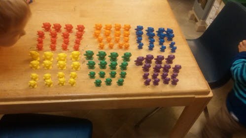 Child looking at colorful bear counters on a wooden table