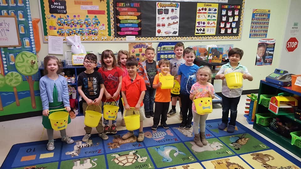 Group of children holding yellow buckets in a classroom