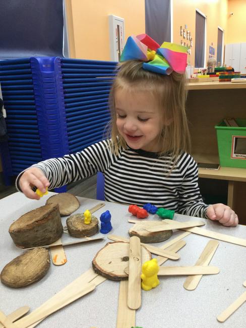 Child playing with wooden discs and small animal figures on a table