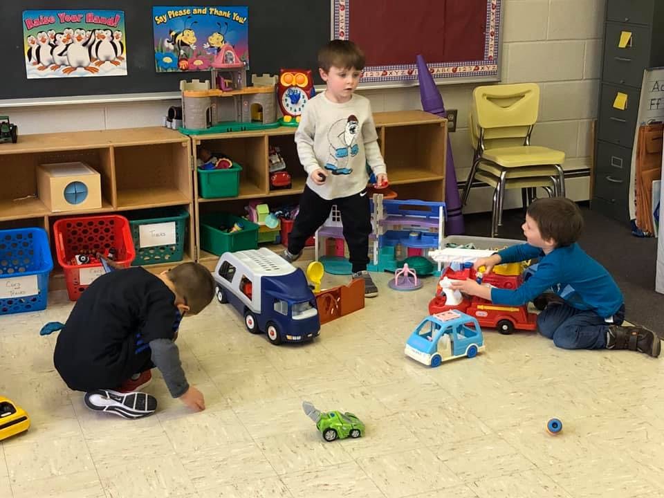 Three children playing with toy vehicles on the floor