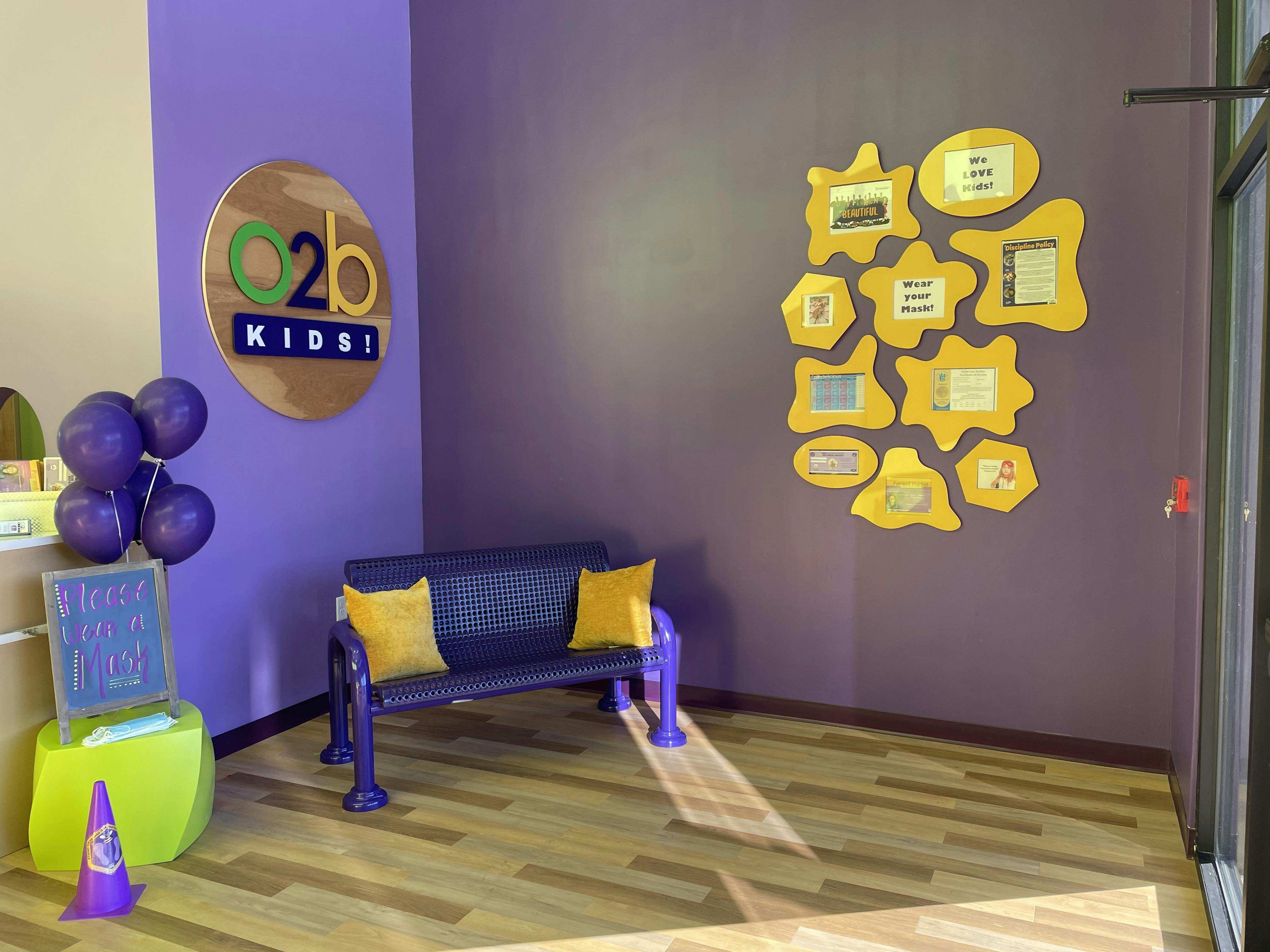 Lobby with a purple bench, yellow cushions, and an O2b Kids sign