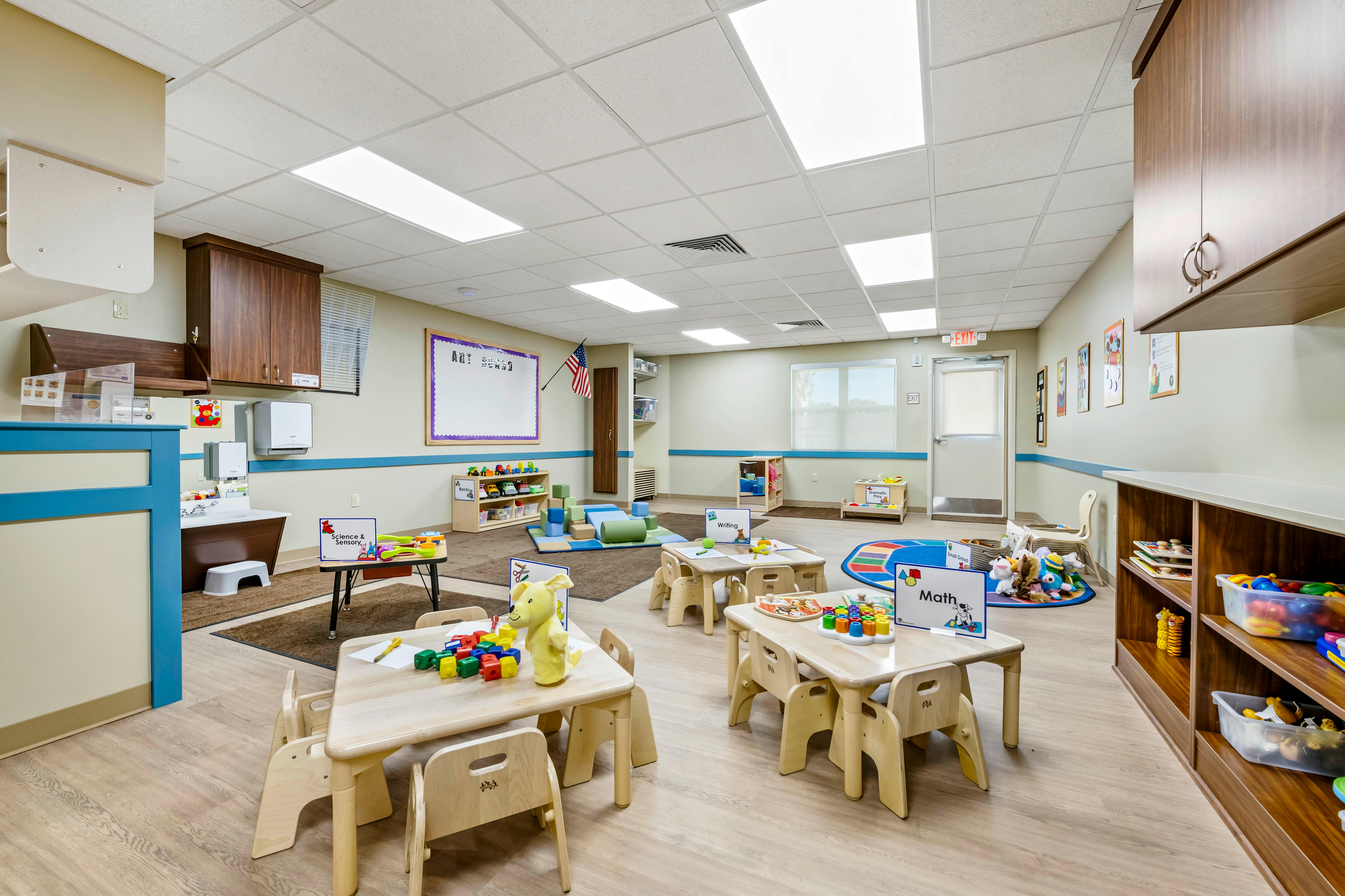 Classroom with small tables and chairs, toys, and activity signs like Science & Sensory and Math