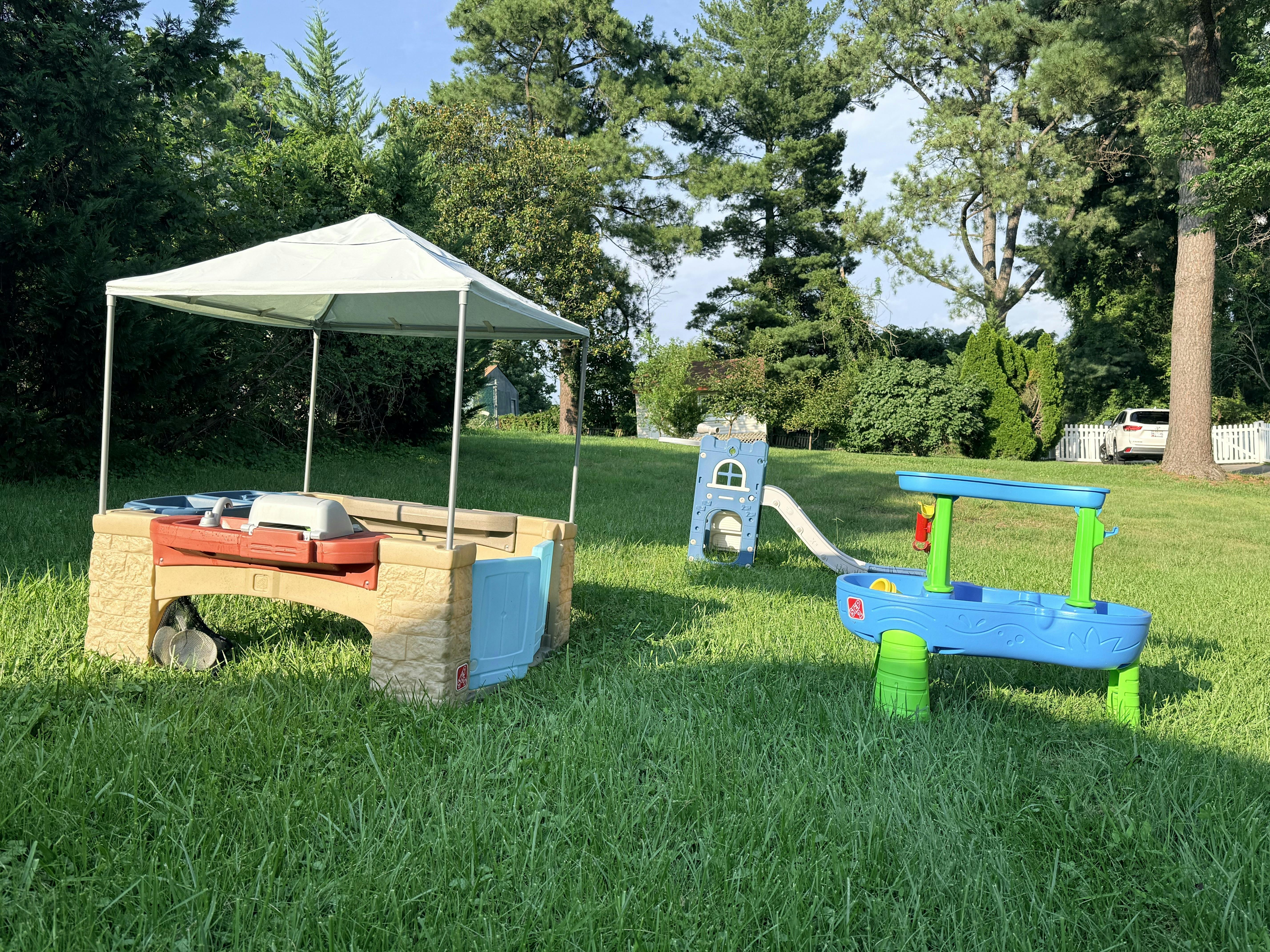 Plastic play equipment including a sand table and water station in a grassy yard