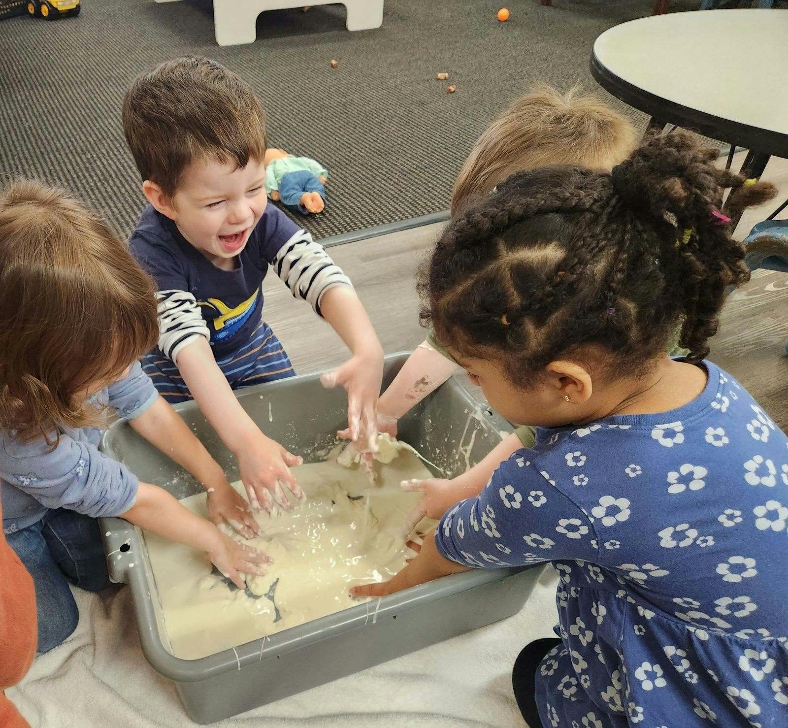 Three children playing with a sensory bin filled with a liquid substance
