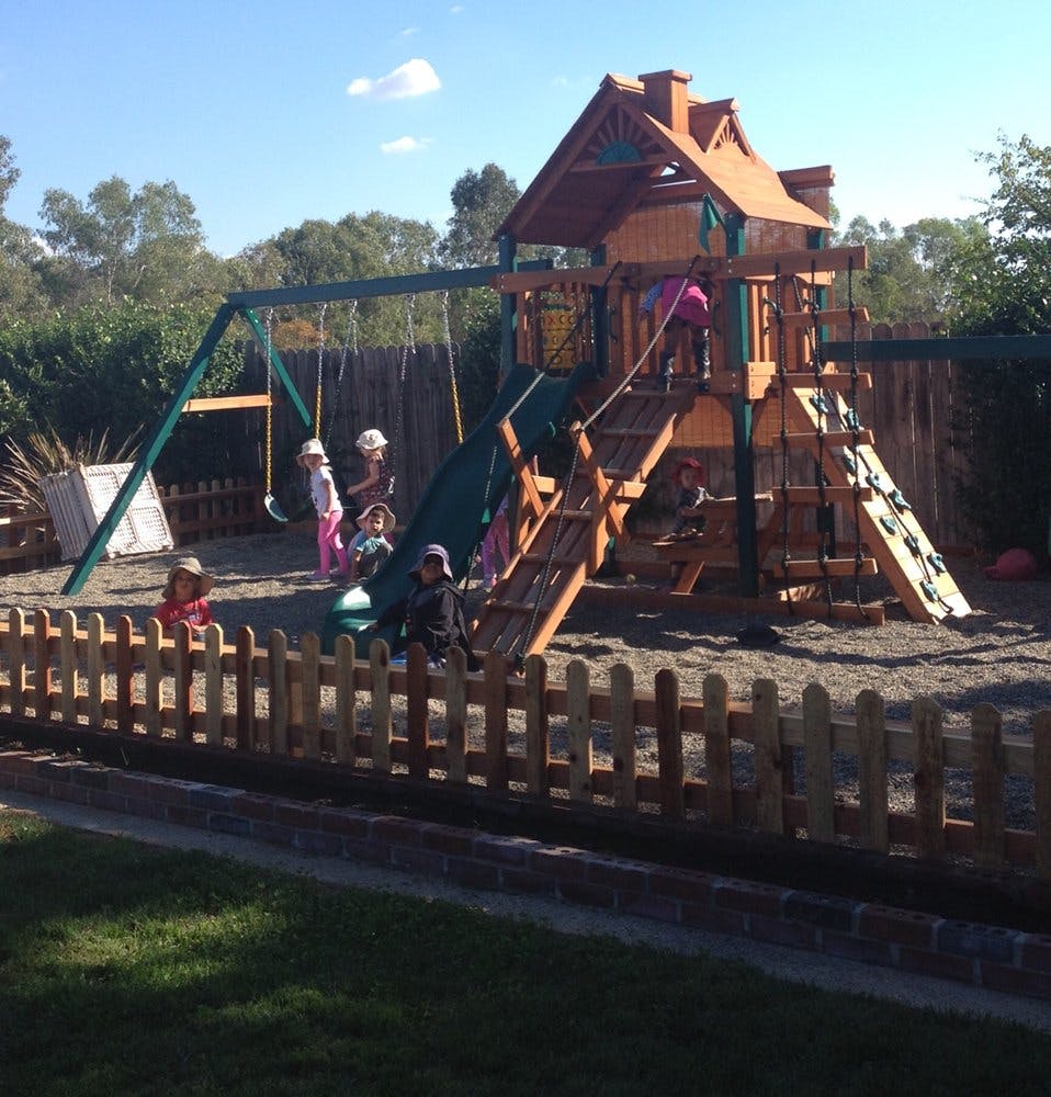 Children playing on a wooden playground structure with swings and a slide