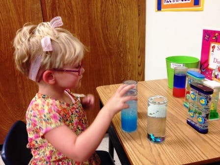 Child with glasses reaching for a glass with blue liquid