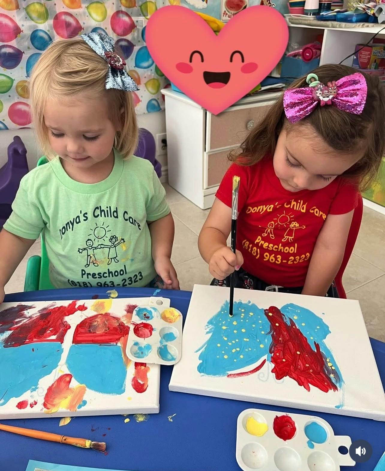 Two children painting on canvases at a blue table