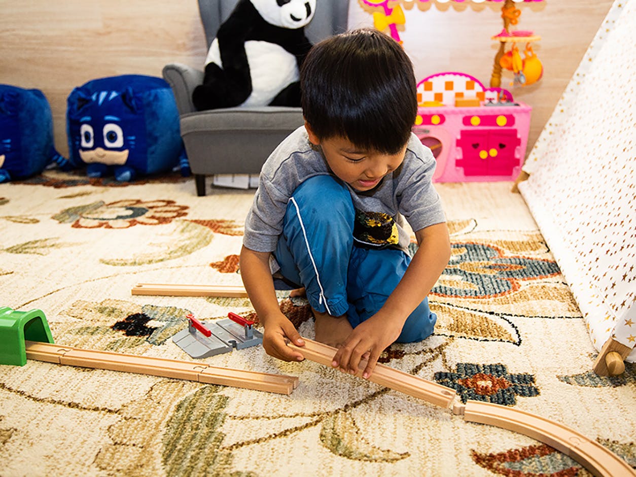 Child playing with a wooden train track on a rug