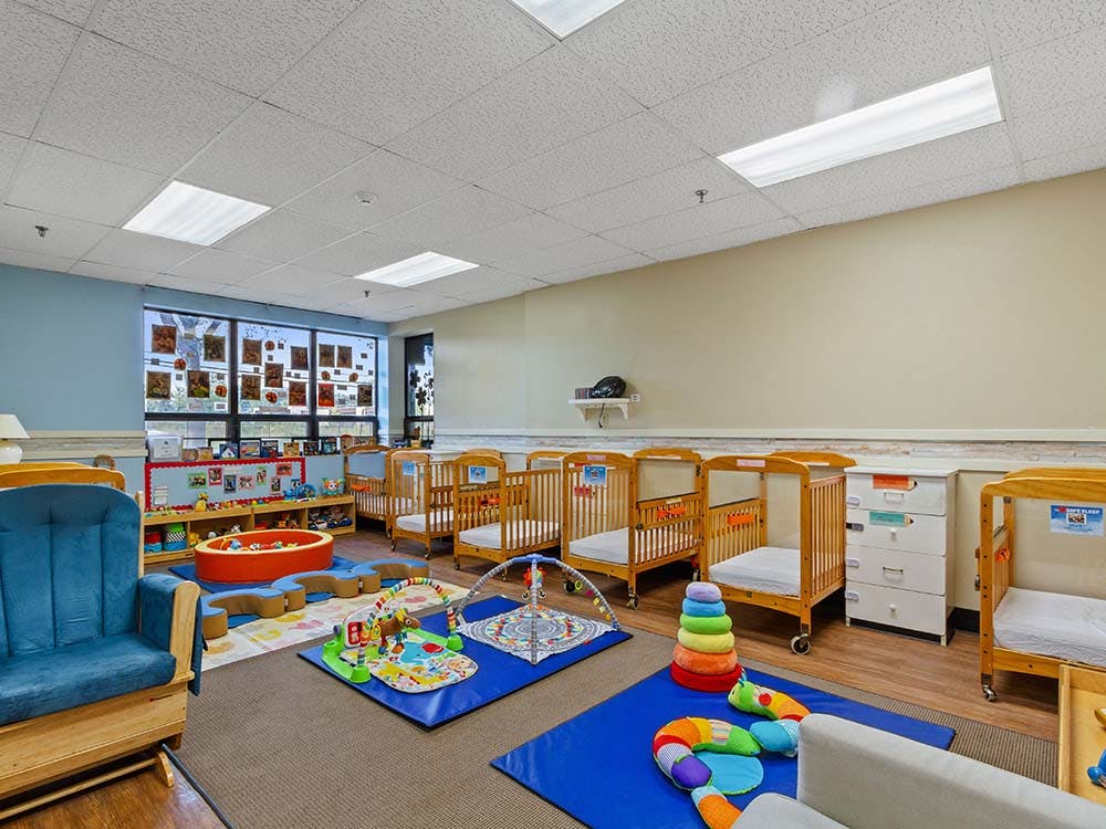 Baby room with cribs, play mats, and a blue rocking chair