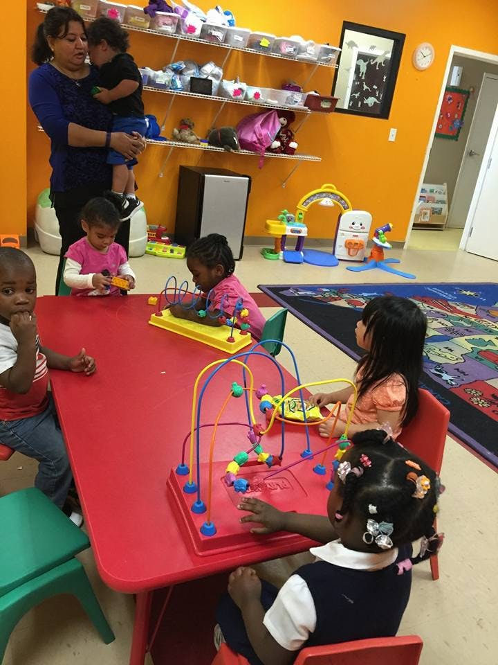 Adult holding a child while other children play with toys at a red table