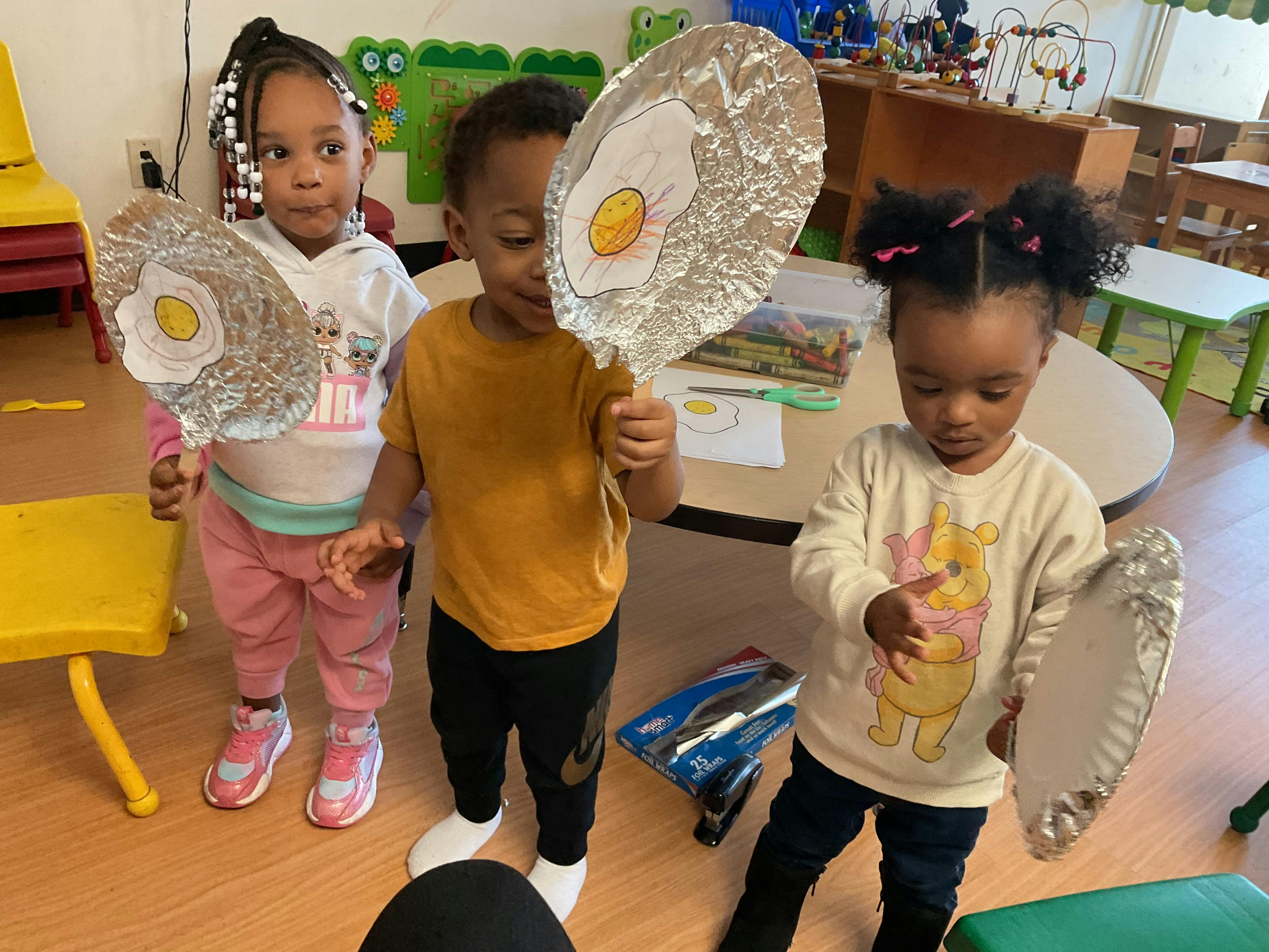 Three children holding up craft projects that look like fried eggs