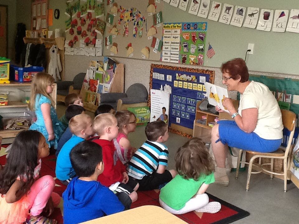 Adult reading a book to a group of children in a classroom
