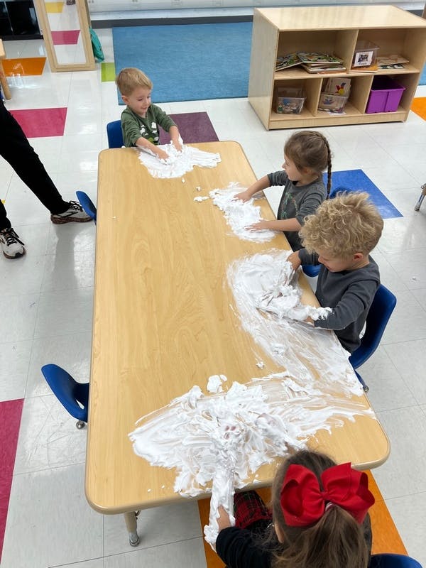 Children playing with shaving cream on a table in a classroom