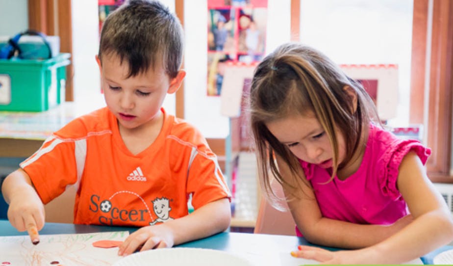 Two children at a table, one pointing at something on paper