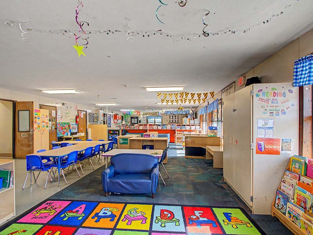 Children's classroom with small tables and chairs, a play rug, and bookshelves