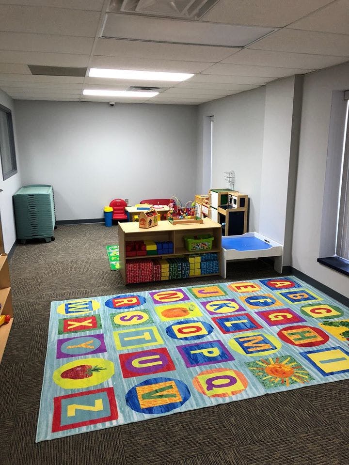 Playroom with an alphabet rug, toy shelves, and small tables