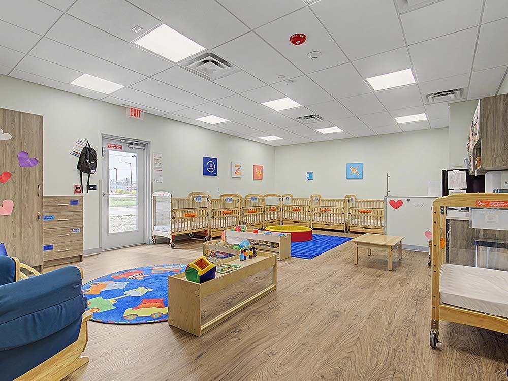 A childcare room with multiple cribs, a colorful rug, and child-sized furniture