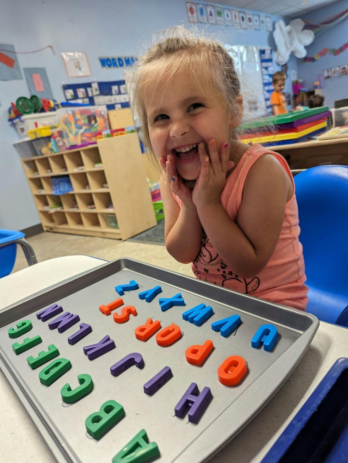 Child with hands on face looking at a tray of alphabet letters