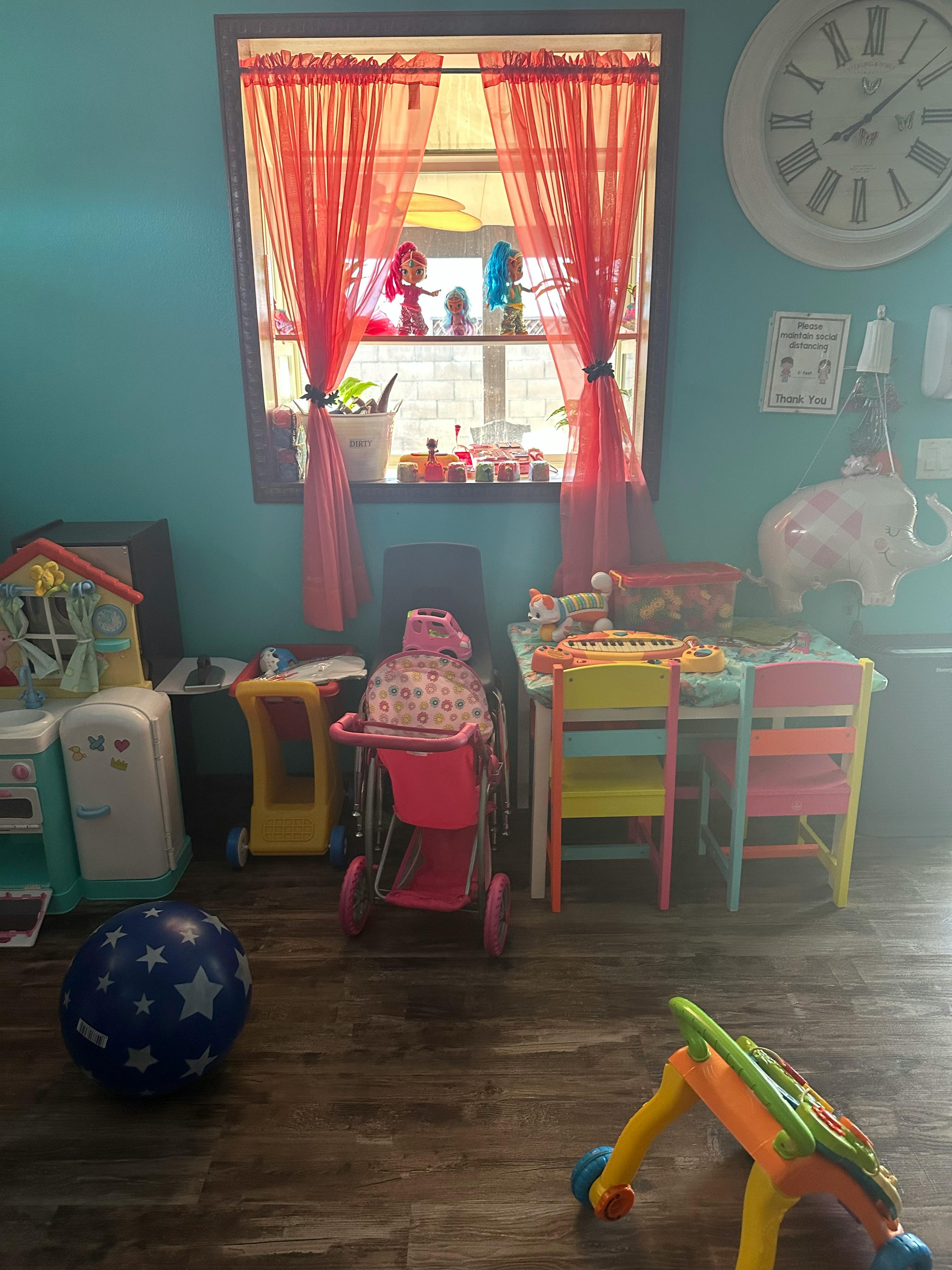 Playroom with toys, a small table and chairs, and a window with red curtains