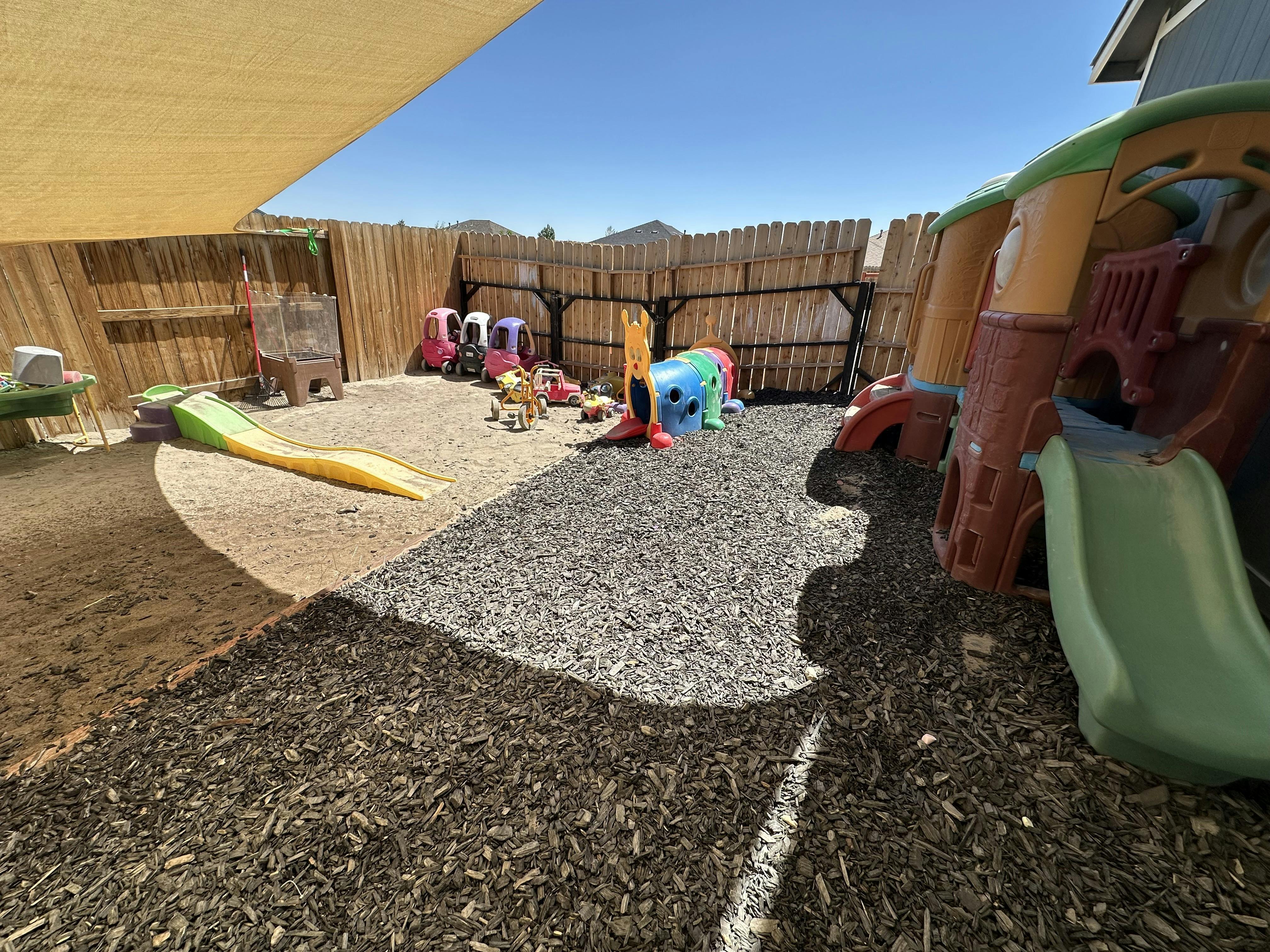 Outdoor children's play area with sand, wood chips, slides, and ride-on toys