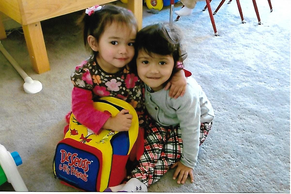 Two children sitting on the floor, one with arm around the other