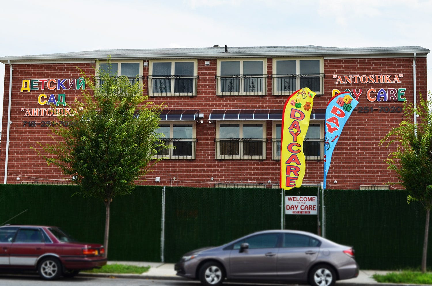 Brick building with "Antoshka Day Care" sign and two cars parked in front