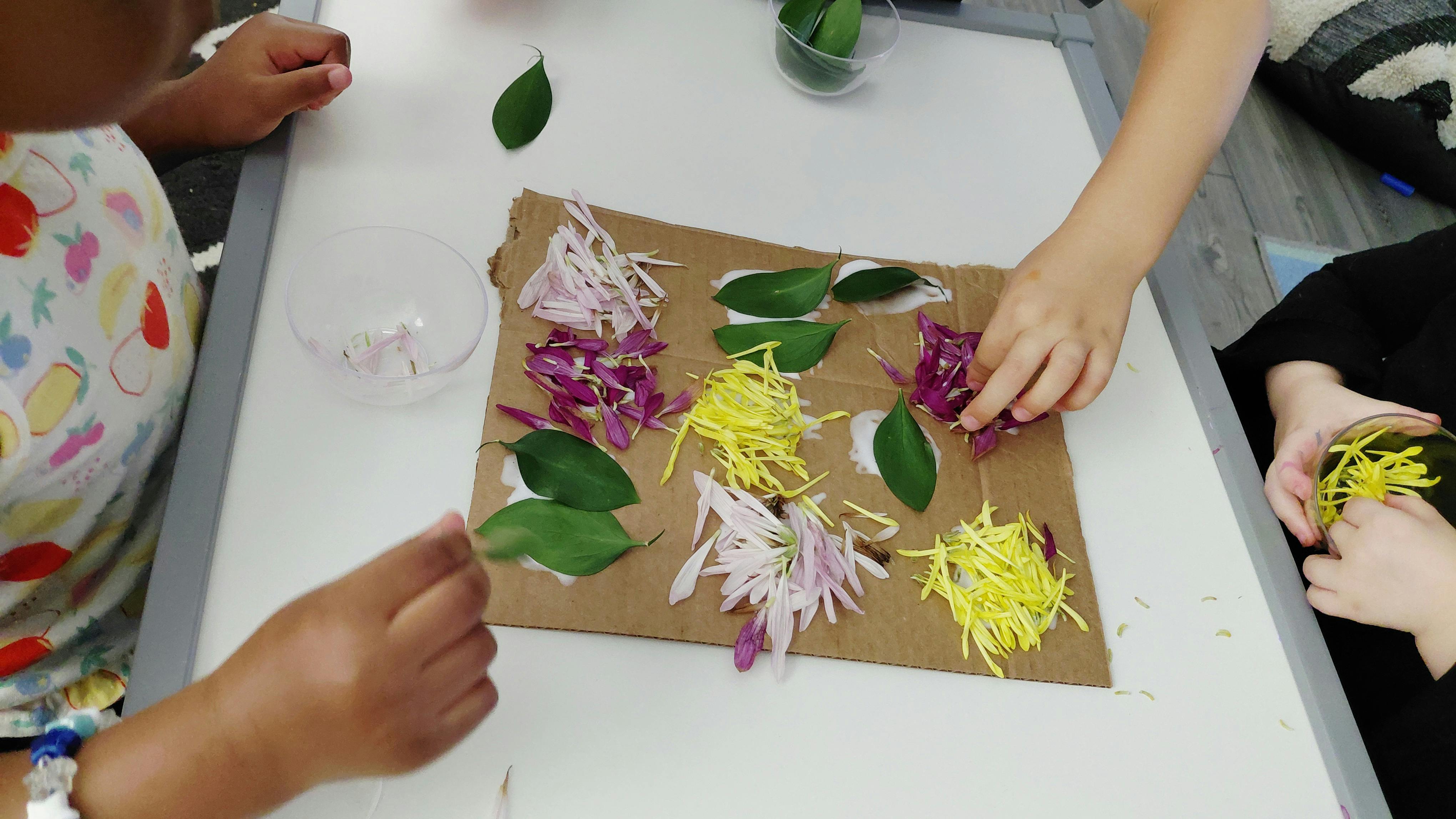 People arranging leaves and flower petals on a cardboard sheet