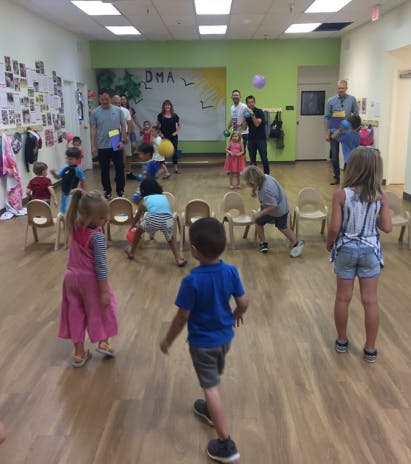 Children and adults playing with balls in a room with small chairs