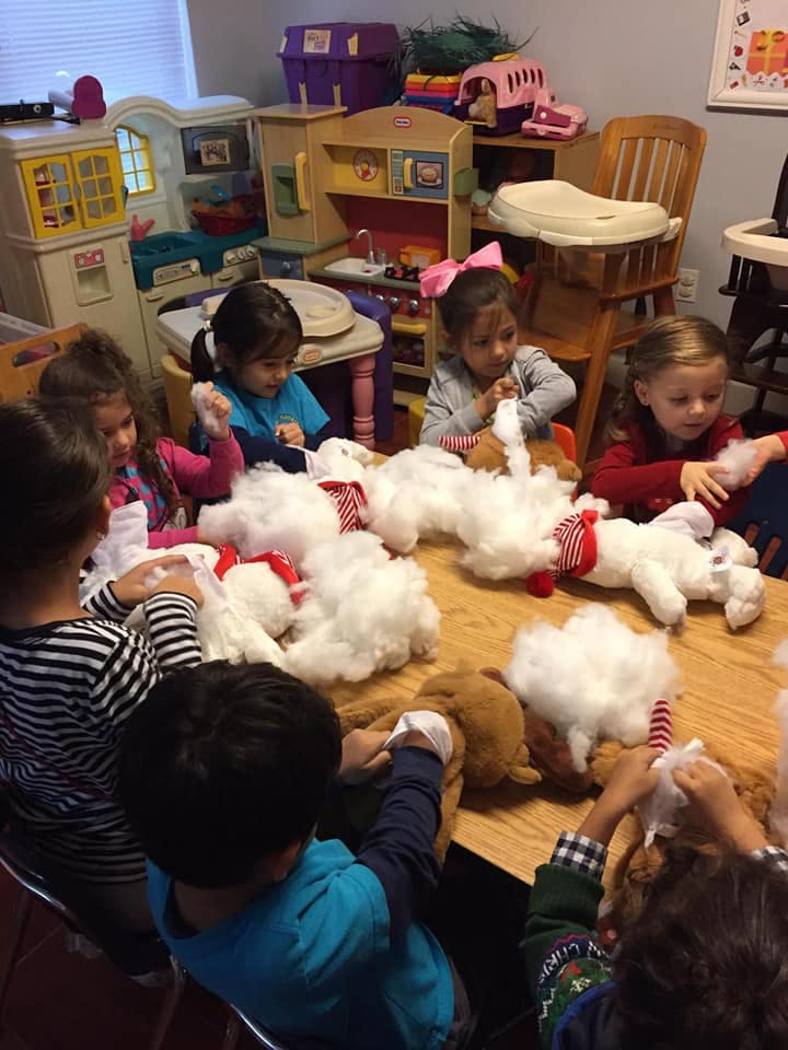 Children stuffing plush toys with white filling at a table