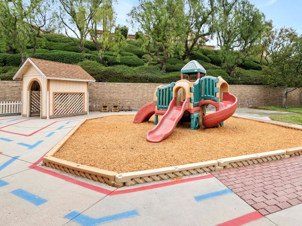 Playground with slides on wood chips next to a small playhouse