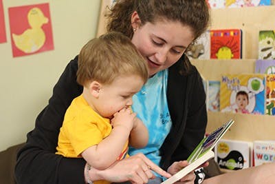 Person holding a child and pointing to a book