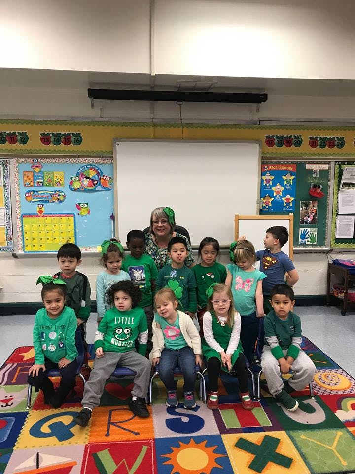 Adult and children in green shirts posing in a classroom