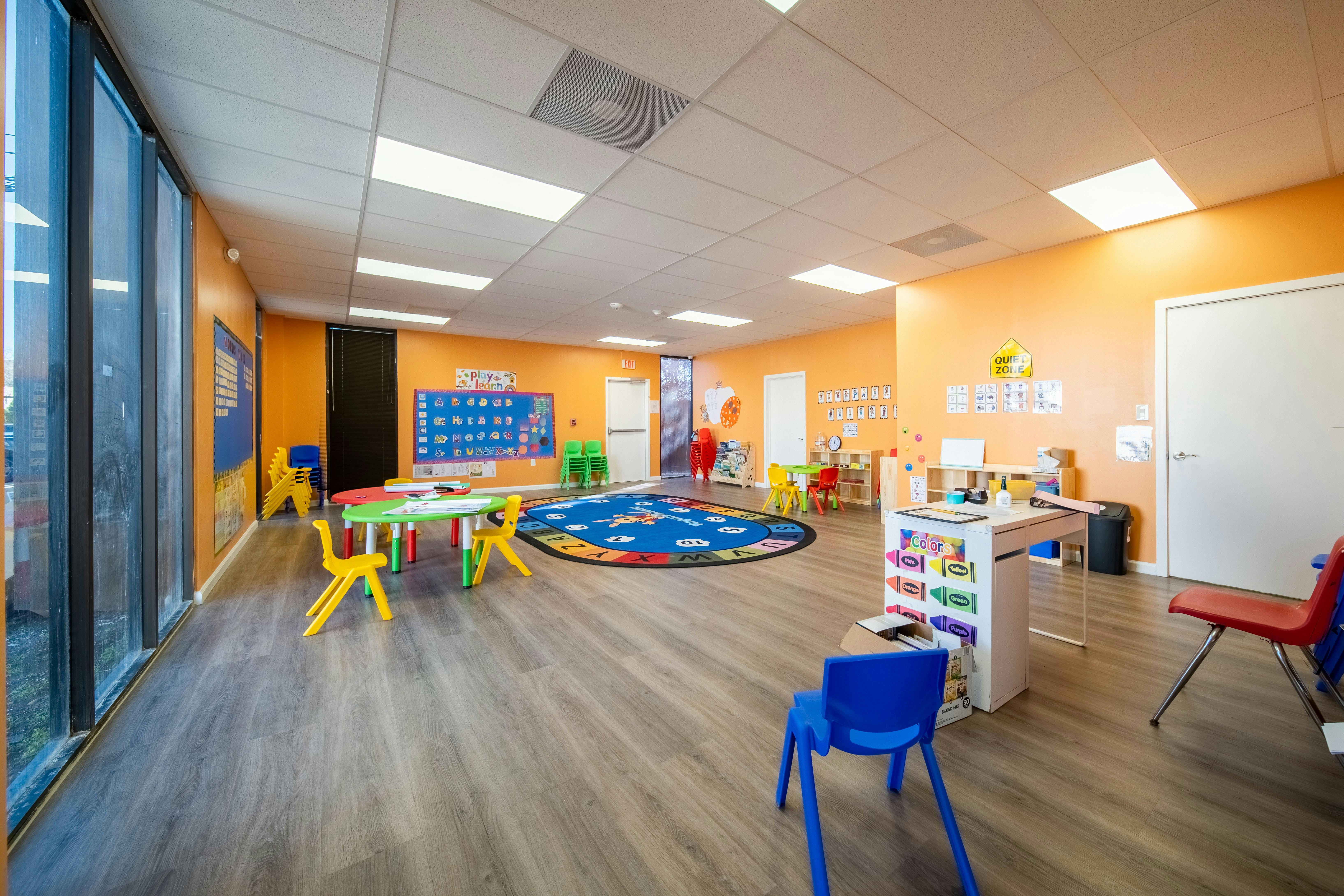 Classroom with colorful tables, chairs, and an alphabet rug