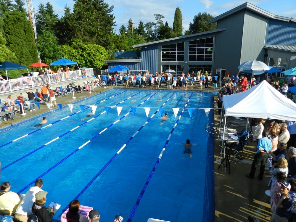 People gathered around an outdoor swimming pool with swimmers in the lanes