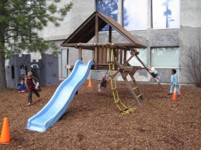 Children playing on a wooden playground structure with a blue slide