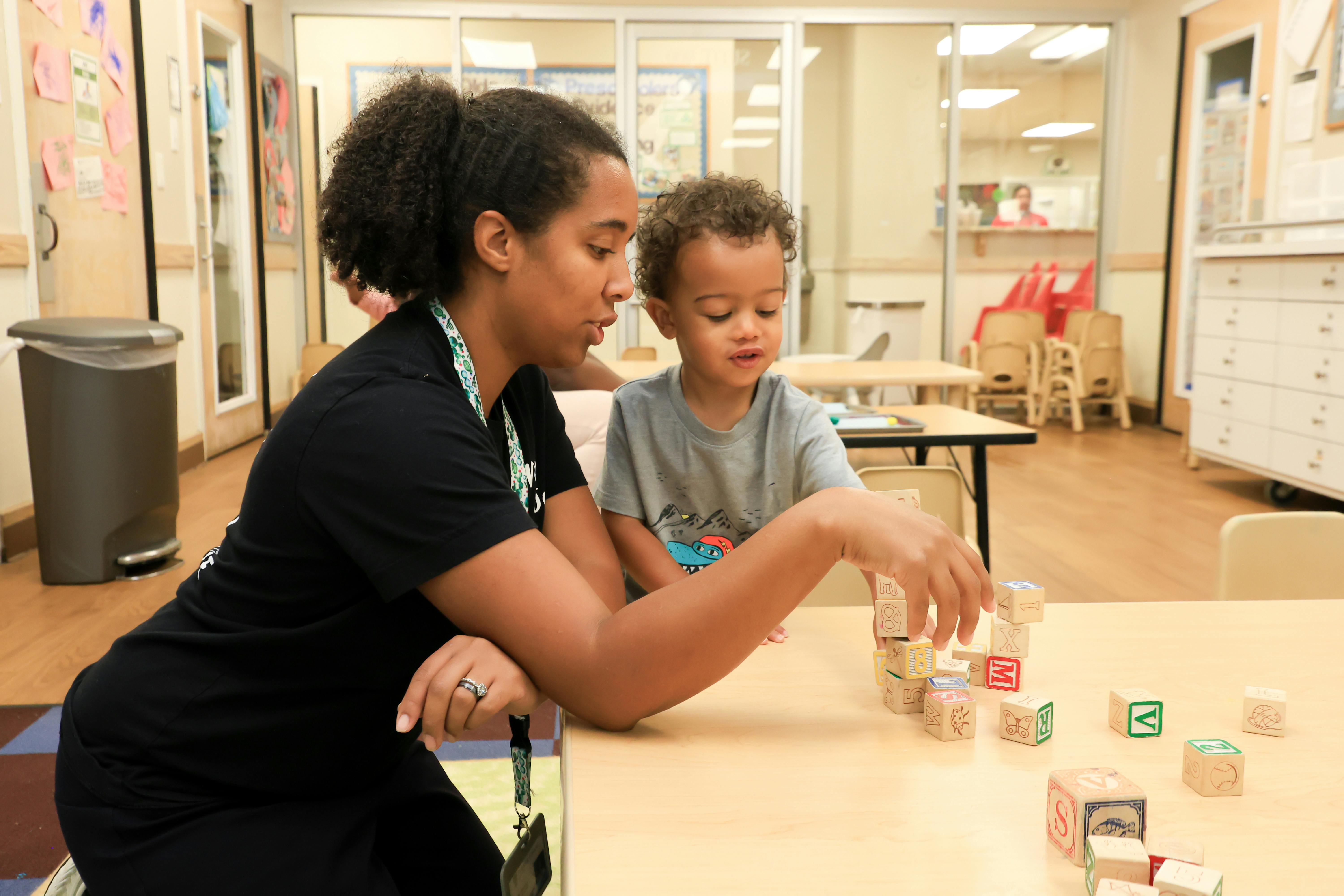 Adult and child playing with blocks at a table in a classroom