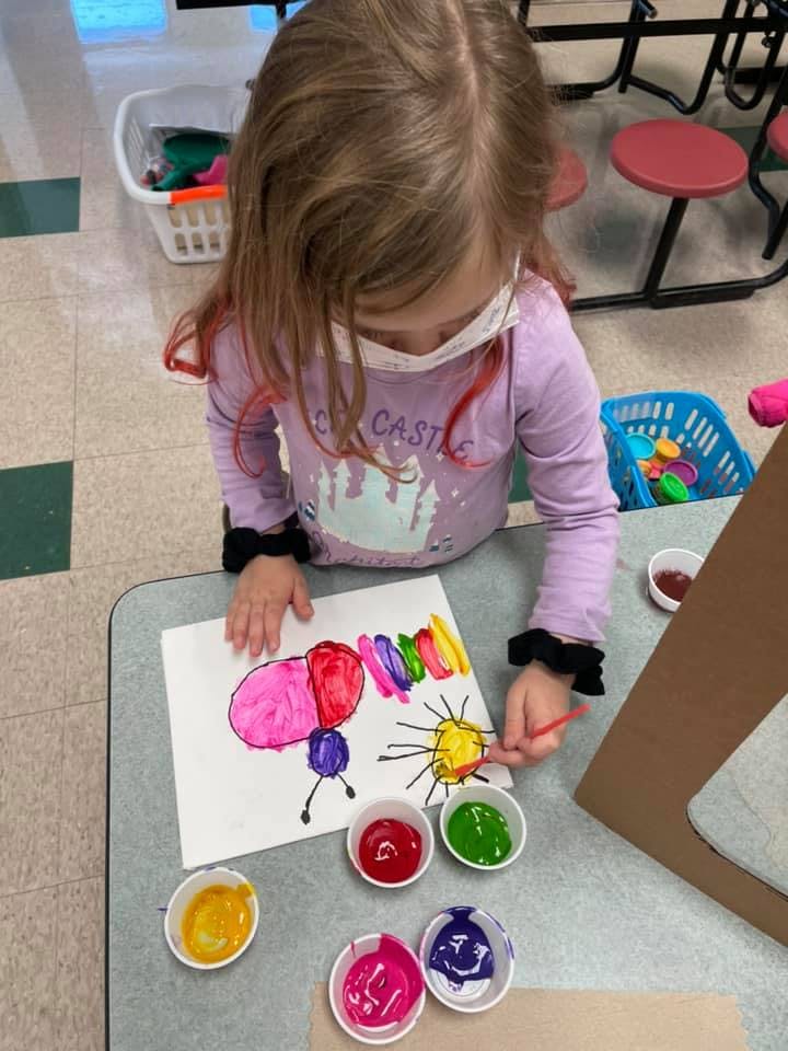 Child painting a colorful butterfly on paper in a classroom