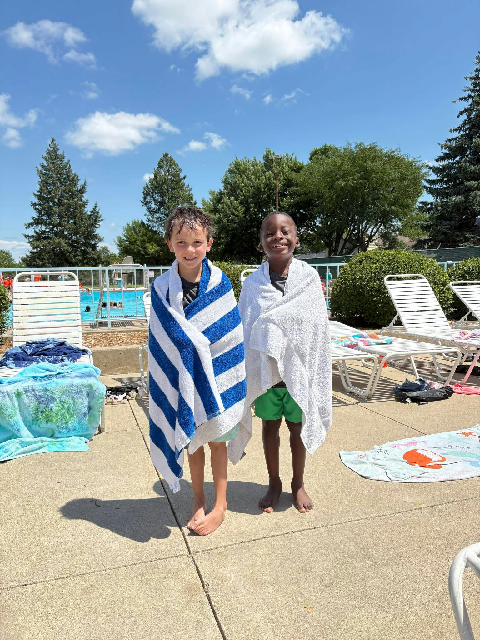 Two children wrapped in towels standing by a swimming pool