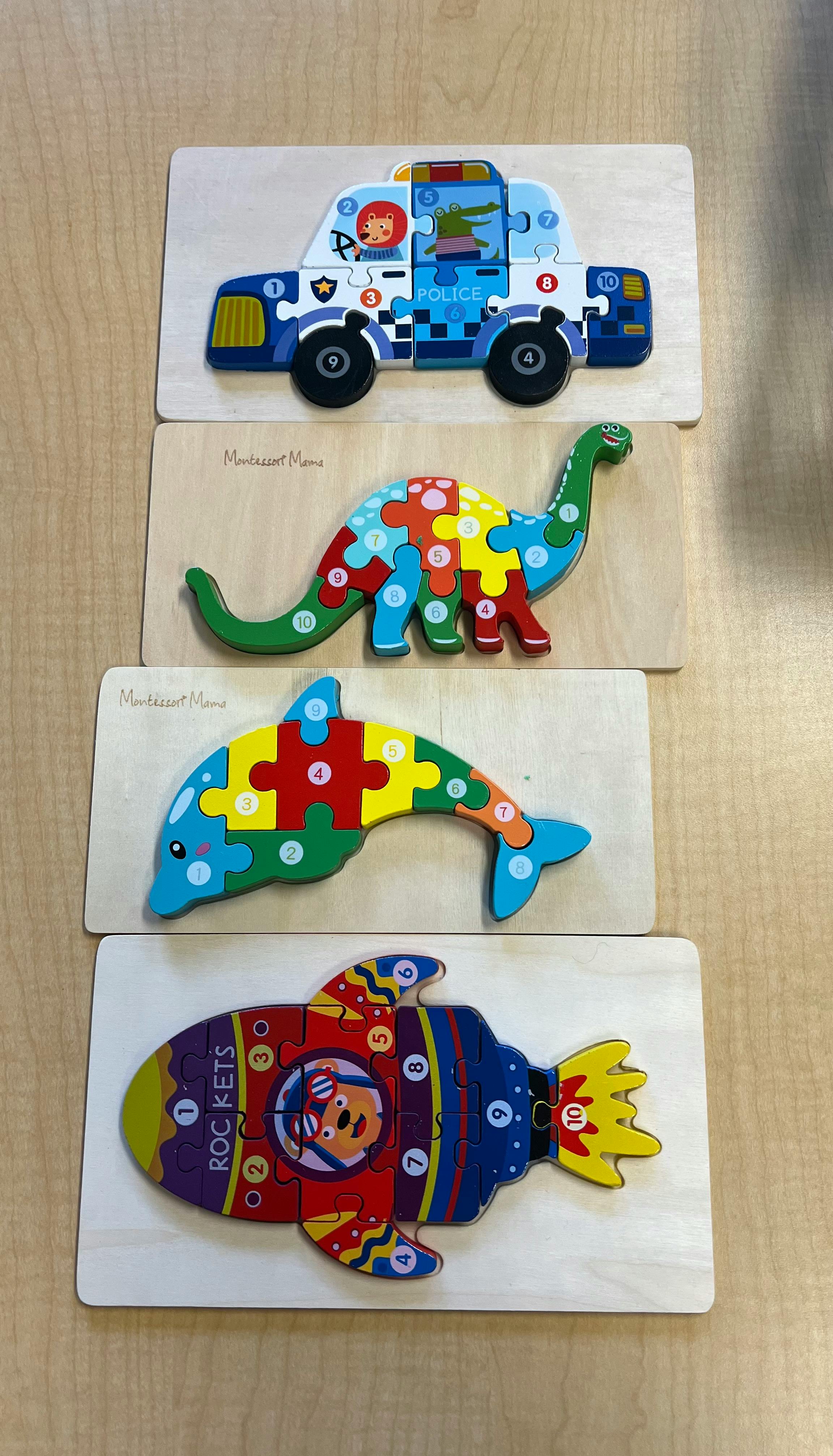 Four wooden puzzle boards with a police car, dinosaur, dolphin, and rocket